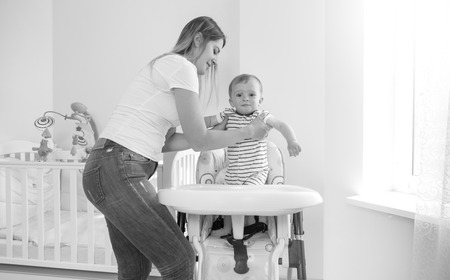 Black and white image of oyung mother seating her baby son in highchair for feedingの写真素材