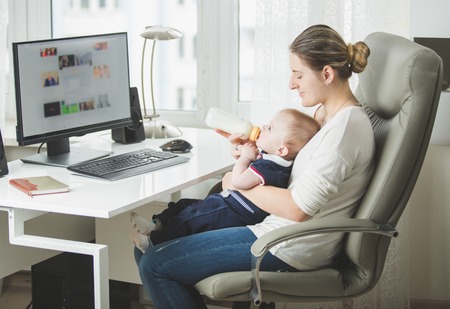 Beautiful young woman working in office and looking after her baby sonの写真素材