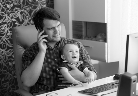 Black and white portrait of young man working in office talking by phone and holding his baby sonの写真素材