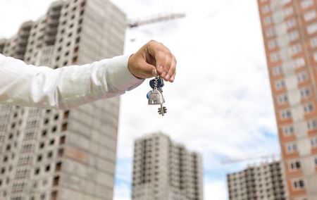 Closeup image of businessman hand holding keys from new home against houses under constructionの写真素材