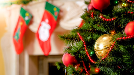 Closeup photo of golden bauble and colorful lights on Christmas tree against mantelpiece