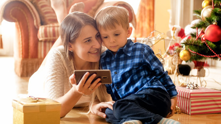 Portrait of smiling mother with her little son watching cartoons on Christmas morningの写真素材