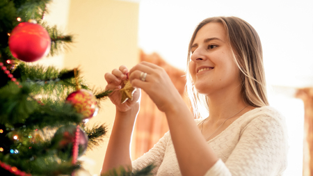 Portrait of smiling young woman putting decorative golden star on Christmas tree branchの写真素材