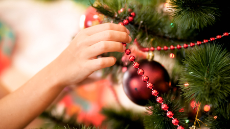 CLoseup photo of female hand putting red decorative beads on Christmas tree branchesの写真素材
