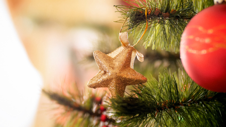 Closeup photo of decorative glittering golden star hanging on Christmas tree branchの写真素材