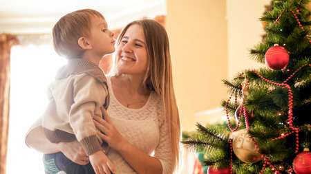 Happy laughing mother holding her little son at Christmas tree in living roomの写真素材