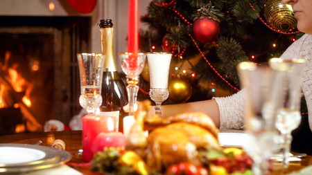 Woman putting glass of champagne on dining table during Christmas family dinnerの写真素材