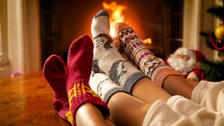 Closeup photo of parents and childs feet in warm woolen socks lying next to burning fireplaceの写真素材