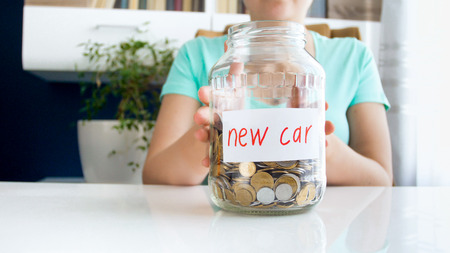Closeup image of young woman holding glass jar full of money for buying new carの写真素材