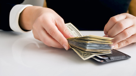 Closeup photo of young businesswoman putting big stack of money in leather wallet