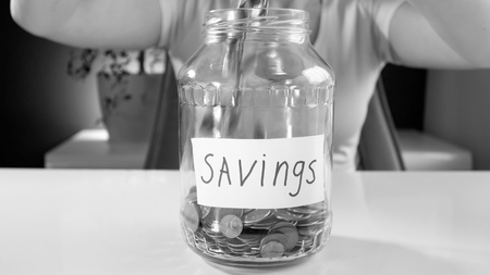 Black and white photo of young woman filling her savings money box wih money