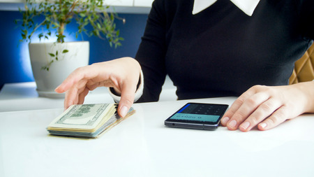 Closeup photo of businesswoman counting money on smartphone calculator