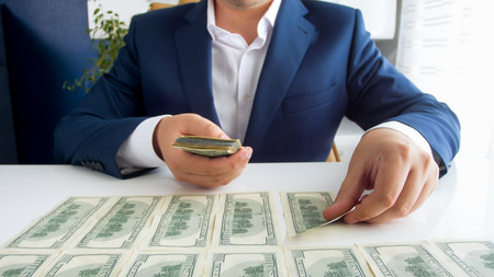 Closeup image of businessman sitting behind desk and laying money in straight rowsの写真素材