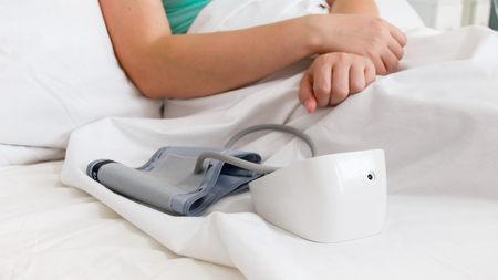 Closeup photo of digital blood pressure monitor in bed of sick woman at hospitalの写真素材