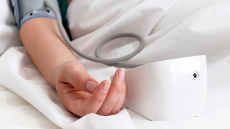 Closeup image of female hand and digital blood pressure monitor on bed
