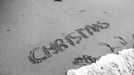 Black and white image of word Christmas written on wet san on the beach. Sea wave flowing over....