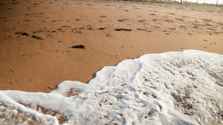 Closeup photo of sea waves rolling over dirty sand on the deserted beach at sunsetの写真素材