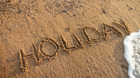 Closeup image of sea waves rolling over word holiday written on beach sand.の写真素材