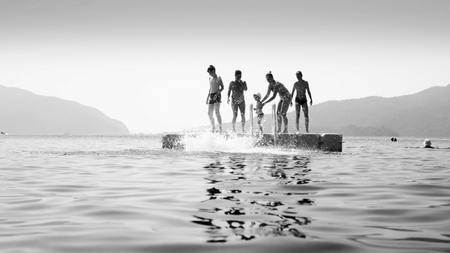 Black and white photo of young people jumping from floating pontoon in calm seaの写真素材