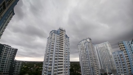 Panoramic photo of dark sky covered with gray and black rain clouds over high living building in city. Cityscape before the stormの写真素材