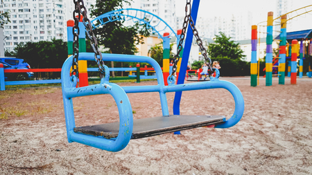 Closeup photo of empty swing hanging on chains on the children playground at parkの写真素材