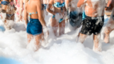 Defocused photo of happy people dancing together on beach. Friends having soap foam sea beach disco party.の写真素材