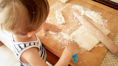 Portrait of cute making dough on wooden kitchen counterboard. Child baking pies or cookies for nreakfastの写真素材