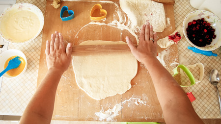 View from top on young woman making dough and rolling it with wooden rolling pin on kitchen...