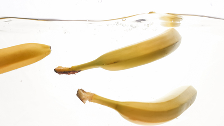 Closeup image of fresh ripe yellow bananas falling and splashing in clear water against isolated white backgorundの写真素材