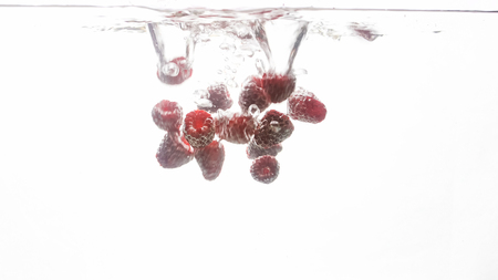 Closeup photo of lots of fresh ripe raspberries falling and splashing in water against white backgroundの写真素材
