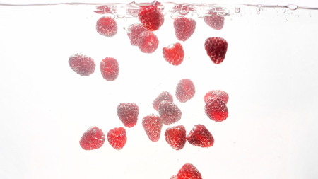 Closeup photo of lots of fresh ripe tasty red raspberries flaoting with air bubbles in clean water...