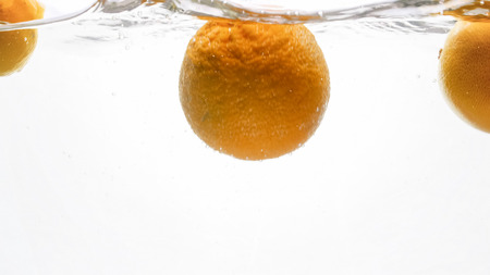 Closeup photo of fresh ripe oranges falling and splashing in water against white backgroundの写真素材