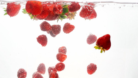 Closeup photo of mixed berries falling and spalshing in water. Lots of raspberries and strawberries floating in water against white backgroundの写真素材