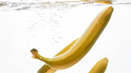 Closeup photo of fresh ripe bananas falling and splashing in water against white isolated backgroundの写真素材