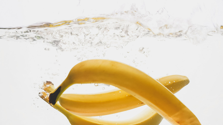 Closeup image of fresh ripe yellow bananas falling and splashing in clear water against isolated white backgorundの写真素材
