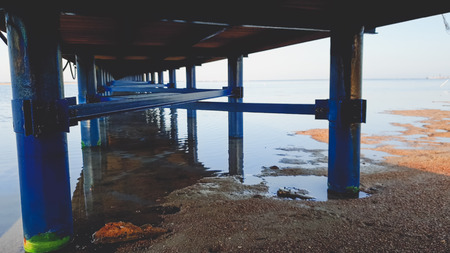 Toned image of long row of metal columns supporting long wooden pier in the sea