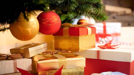 Closeup image of golden and red baubles hanging on Christmas tree over big heap of gifts and...