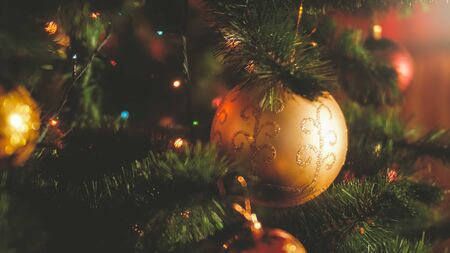 Closeup toned photo of glowing lights and colorful balls on Christmas tree at house. Perfect...