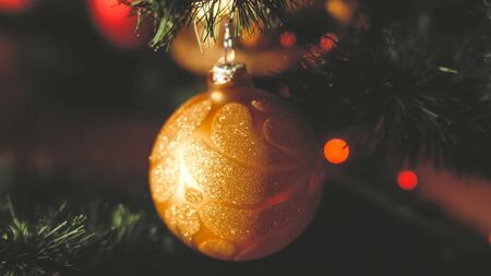 Closeup toned retro photo of golden shiny bauble hanging on Christmas treeの写真素材