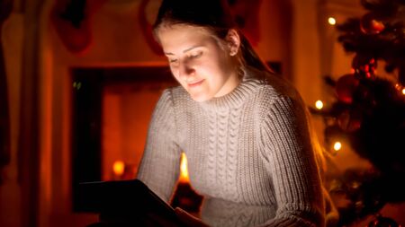 Portrait of young woman in sweater sitting next to the fireplace and using digital tabletの写真素材