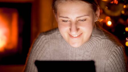 Closeup portrait of happy smiling woman with digital tablet sitting by the fireplace at nightの写真素材