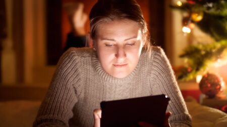 Portrait of young owman lying on the floor next to glowing Christmas tree and holding tabletの写真素材