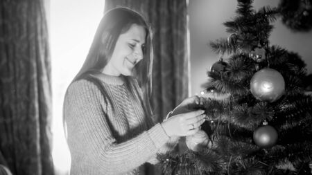 Black and white portrait of smiling young woman decorating Christmas tree at morning