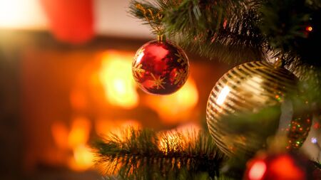 Closeup image of red and golden Xmas baubles hanging on Christmas tree aginst burning fire in...