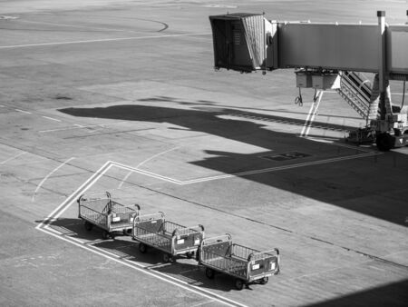 Black and white photo of boarding gate corridor and empty carts for carrying and loading luggage in airplaneの写真素材