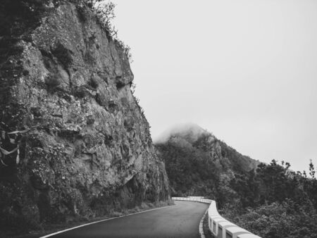 Black and white image of narrow road in the mountains covered with clouds or fogの写真素材