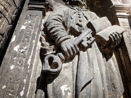 Closeup image of ancient stone sculpture of priest holding a book and key