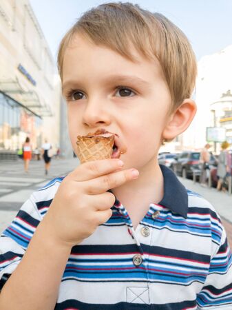 Portrait of little boy with dirty mouth eating chocolate ice cream on streetの写真素材