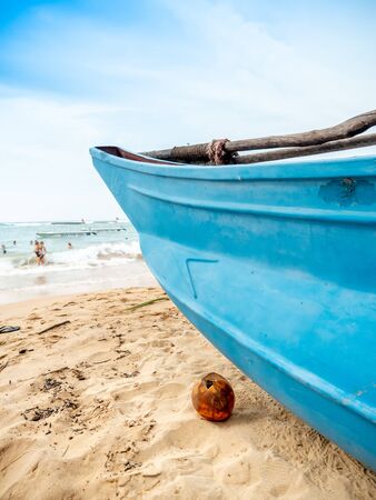 Closeup image of yellow coconut lying on the ocean baech next to old wooden fishing boatの写真素材