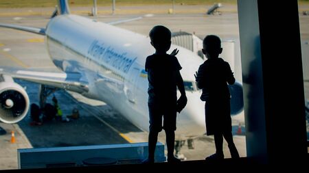Silhouette of two little boys loking through window on airplane in airport terminalの写真素材